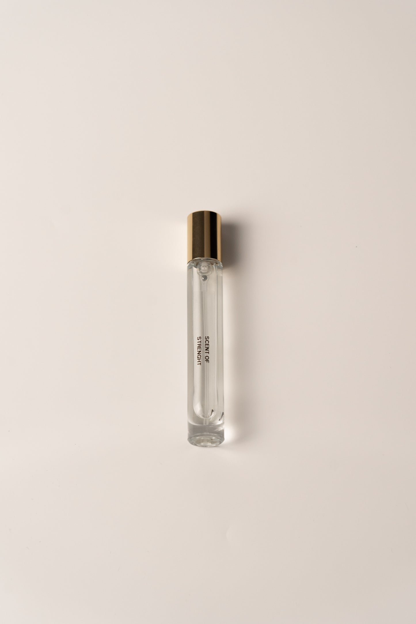 Clear glass perfume bottle with gold cap on a light beige background
