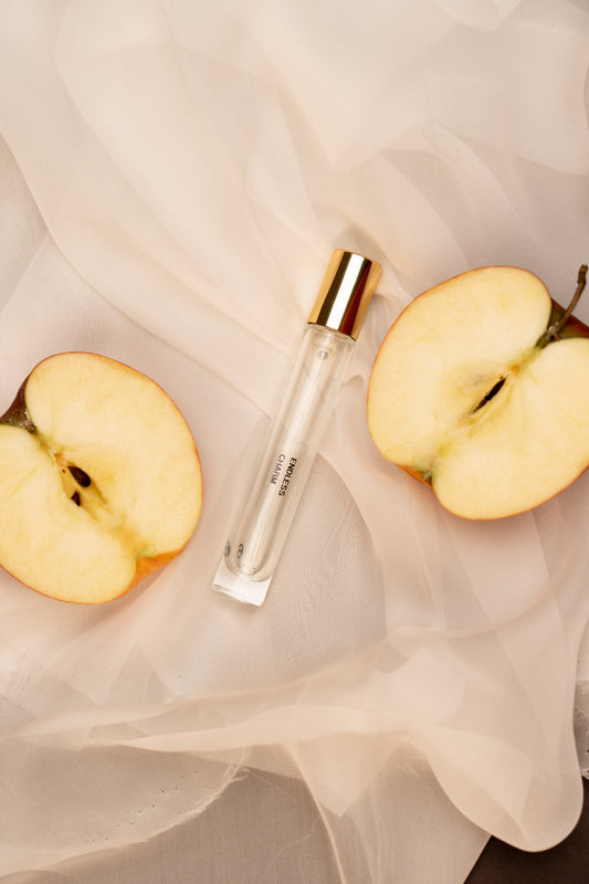 Roll-on perfume bottle with gold cap and clear container on a light fabric background with sliced apples.